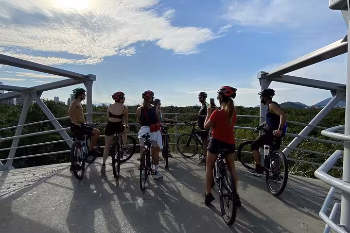 Group of cyclists on a Florianopolis bridge enjoying scenic views during a photography and street food bike tour.
