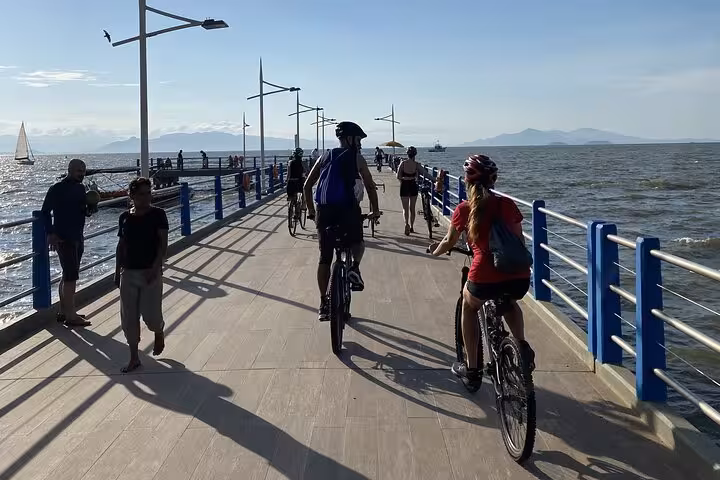 Cyclists explore a seaside pier in Florianopolis, combining photography, history, and street food on a sunny day.