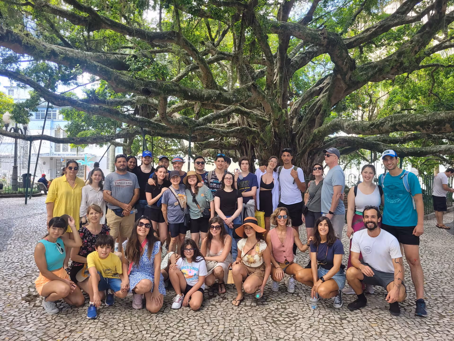 Group of tourists posing under a large tree during a Florianopolis walking tour highlighting history and art.