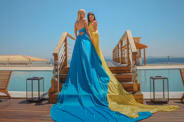 Two women in stunning blue and yellow dresses pose on a wooden deck overlooking the sea at the Port of Heraklion, Greece.