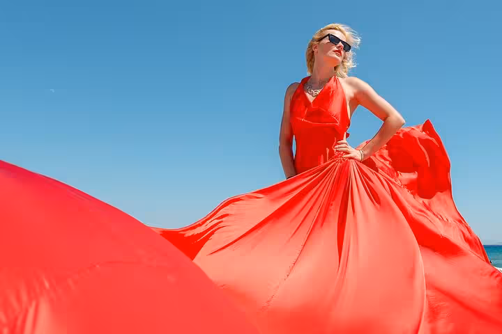Woman in a flowing red dress poses confidently against a clear blue sky at the Port of Heraklion, perfect for a flying dress photoshoot.