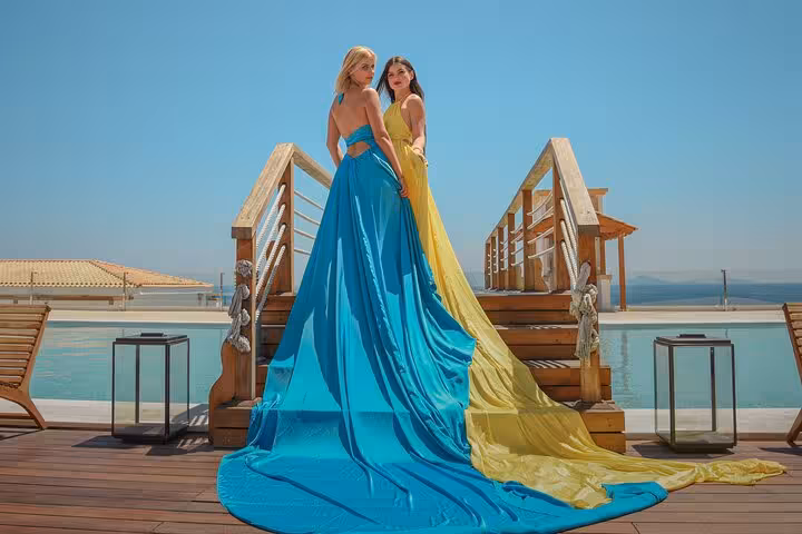 Two women in flowing blue and yellow dresses stand on a wooden deck by the pool in Hersonissos for a unique photoshoot.