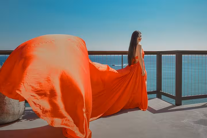 Elegant woman in vibrant red dress enjoys breathtaking sea view during flying dress photoshoot in Hersonissos.