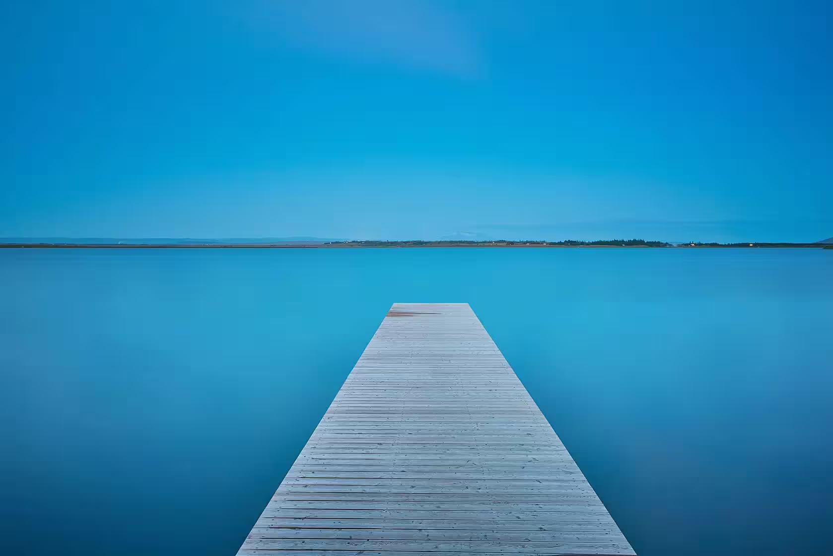 Wooden dock extending over calm turquoise lake under clear blue sky near Fontana Spa Iceland
