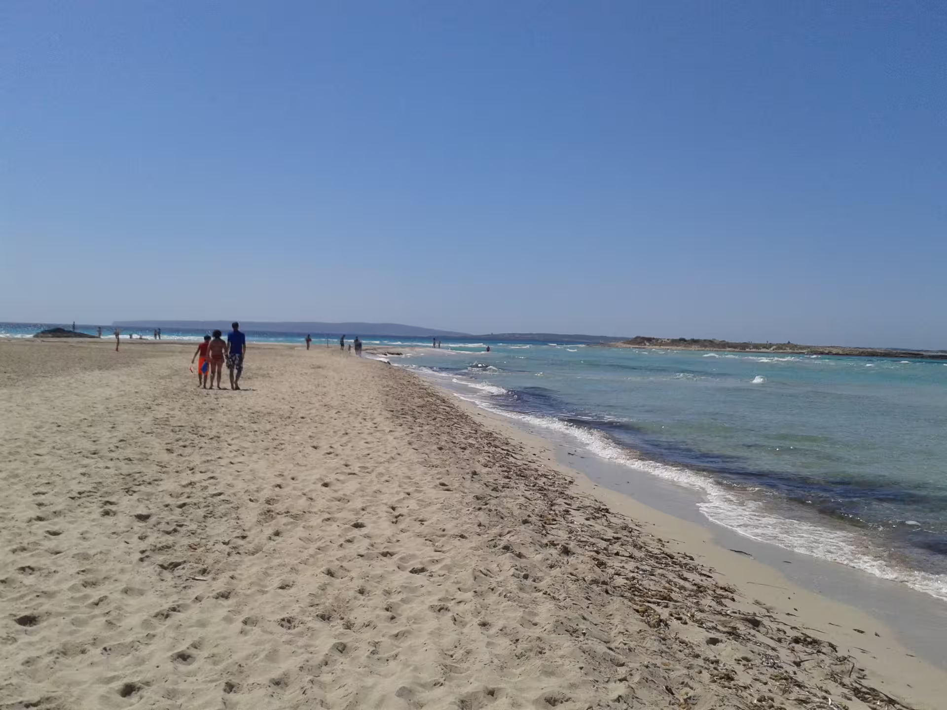 People walking along Formentera shoreline with clear water, featured on Ibiza day trip with transfers and ferry