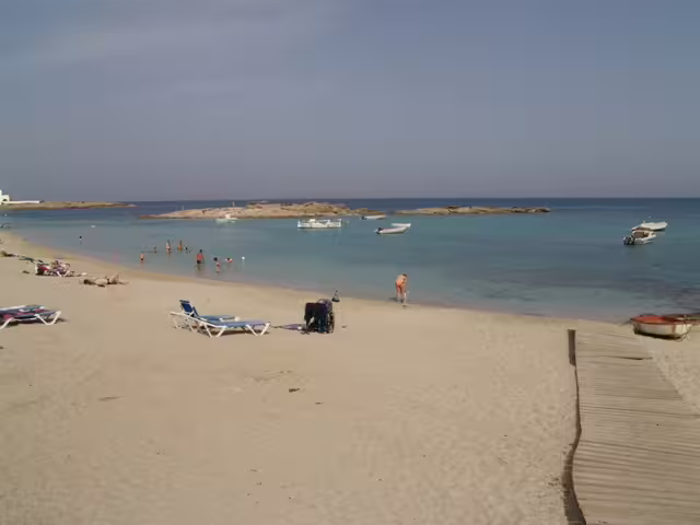 Sandy Ibiza beach with calm turquoise water and boats, scenic stop on Ibiza bus tour with fast ferry and guide