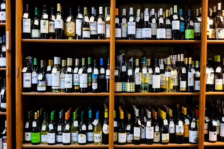 Assorted bottles of fortified wine on wooden shelves, ideal for a tasting experience with a producer in a wine tour setting.