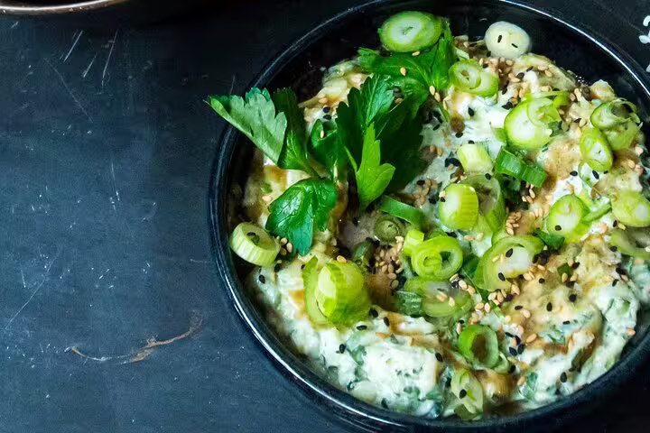 A vibrant dish of creamy dip garnished with fresh parsley, green onions, and sesame seeds, perfect for a wine tasting event.