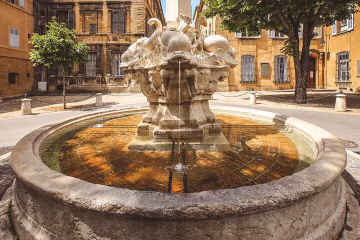 Fountain of the Four Dolphins in a sunlit square in Aix-en-Provence, showcasing historic architecture.