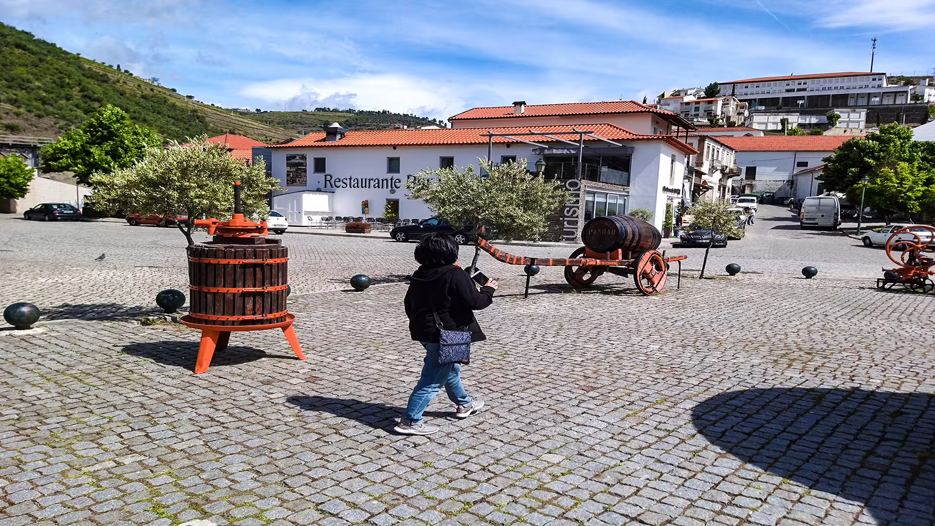 A tourist explores Foz Côa's charming cobblestone streets, surrounded by wine barrels and scenic views on a Douro private tour.