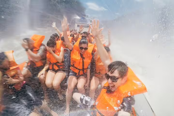 Visitors enjoying a thrilling speedboat ride through the misty waters of Foz do Iguaçu, raising hands in excitement.
