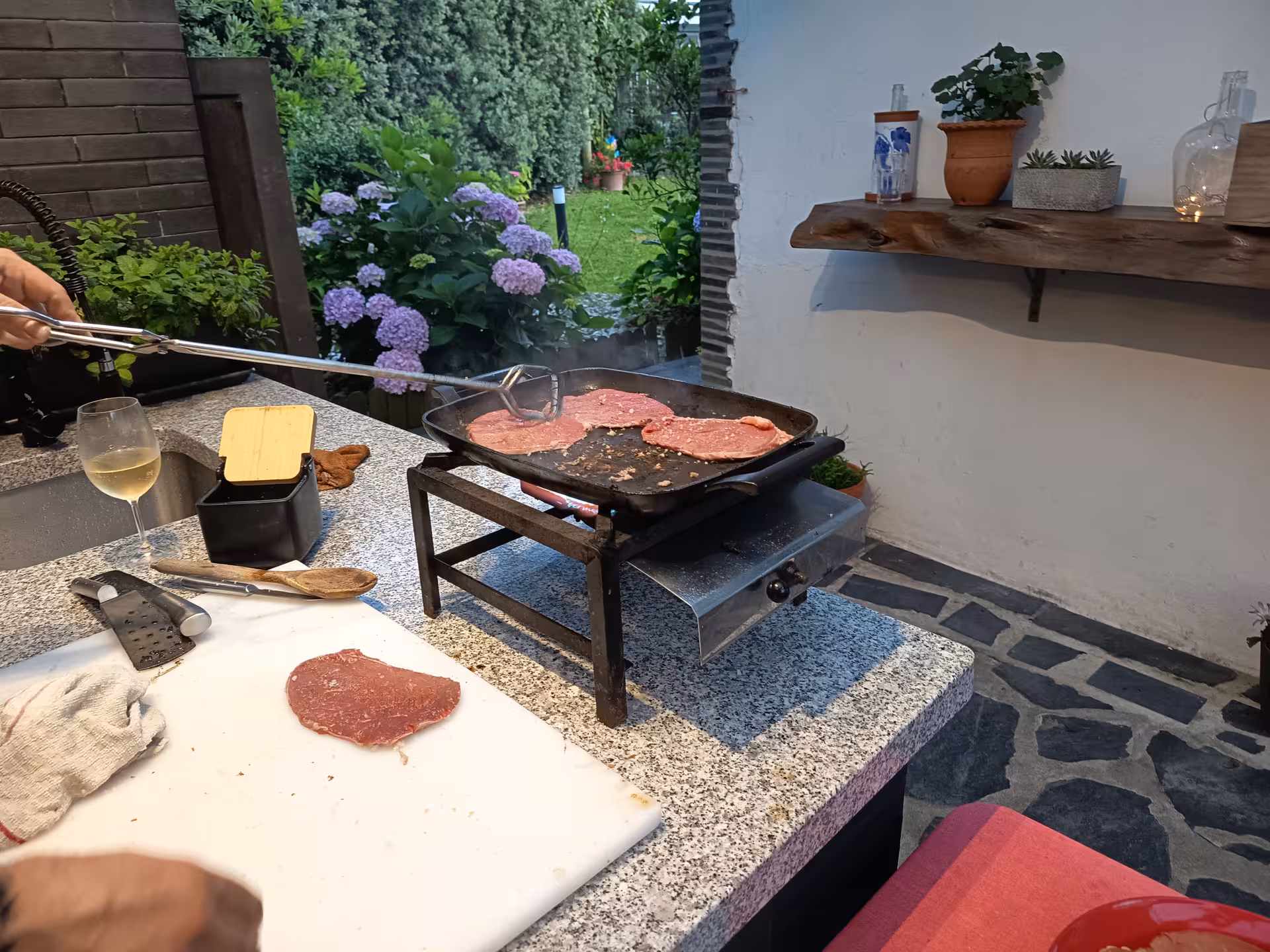 Cooking steaks on a hot grill with garden view during Francesinha preparation experience in Porto.