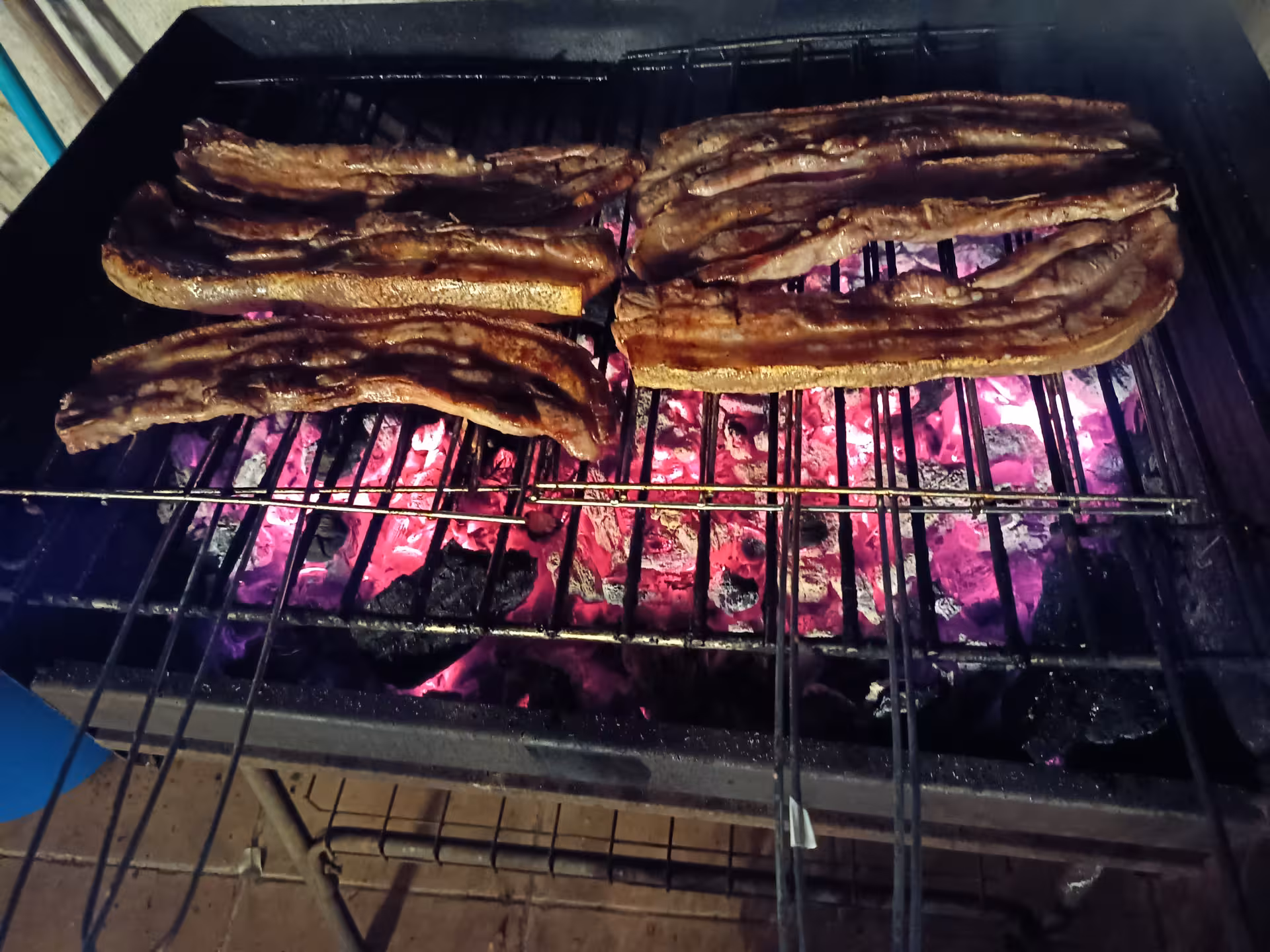Slices of meat grilling over hot coals for a traditional Francesinha preparation experience in Porto.