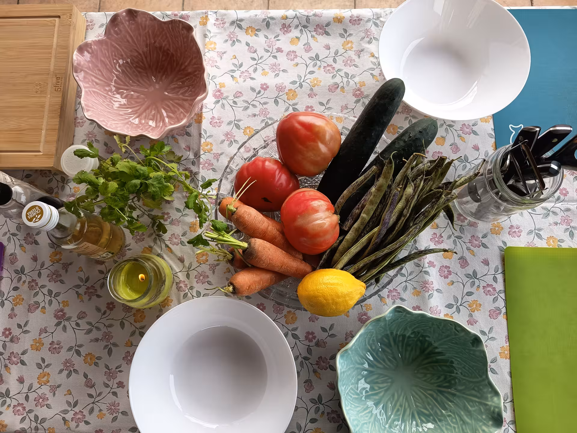 Fresh vegetables and herbs arranged on a floral tablecloth, including tomatoes, carrots, and cucumbers for Porto cooking tour.