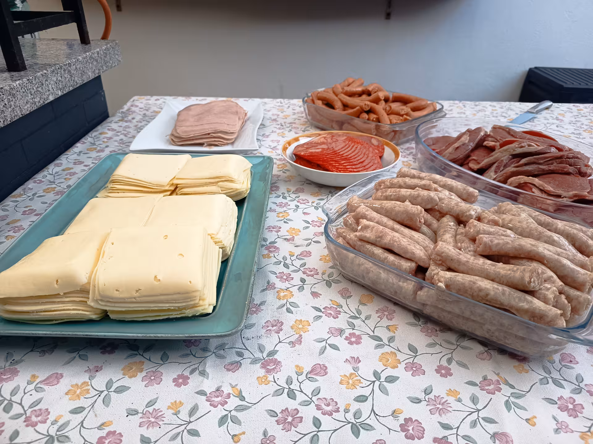 Assorted ingredients for Francesinha in Porto, featuring cheese slices, sausages, and cured meats on a floral tablecloth.