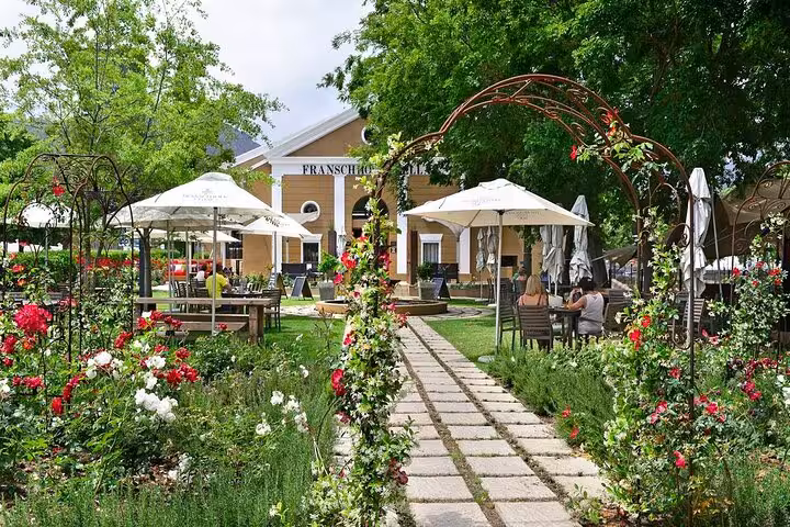 Charming garden entrance with blooming flowers and outdoor dining in Franschhoek, ideal for a Cape Town excursion.