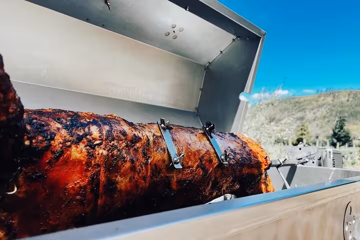 Close-up of a whole roast on a spit under blue skies, offering a taste of local cuisine on a Franschhoek tour.