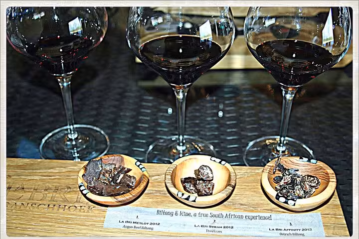Wine tasting experience at Franschhoek with red wine glasses and biltong, highlighting South African flavors.