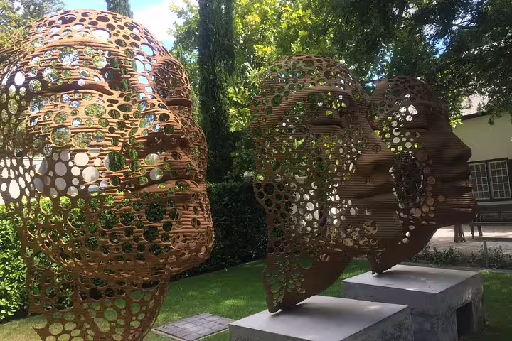 Intricate metal head sculptures in a serene garden setting in Franschhoek wine tour.