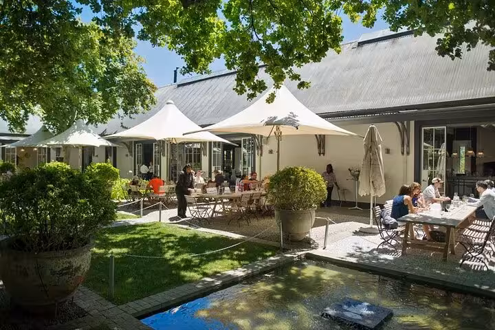 Charming outdoor dining area at a Franschhoek winery with shaded seating, lush greenery, and a tranquil ambiance.