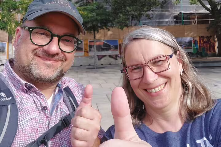 Happy couple giving thumbs up on Freiburg in Breisgau scavenger hunt, self-guided walking tour with puzzles