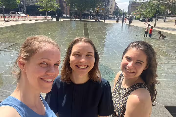 Three friends at Freiburg city fountain on a self-guided scavenger hunt tour, exploring Breisgau sights