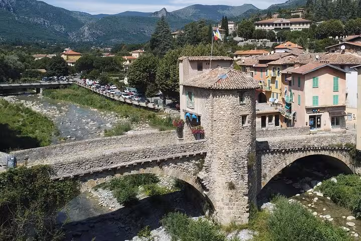 Medieval stone bridge with vibrant village backdrop and scenic river views in the French Alps tour.