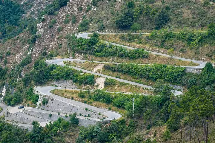 Winding mountain road through lush greenery in the French Alps, perfect for a scenic drive tour.