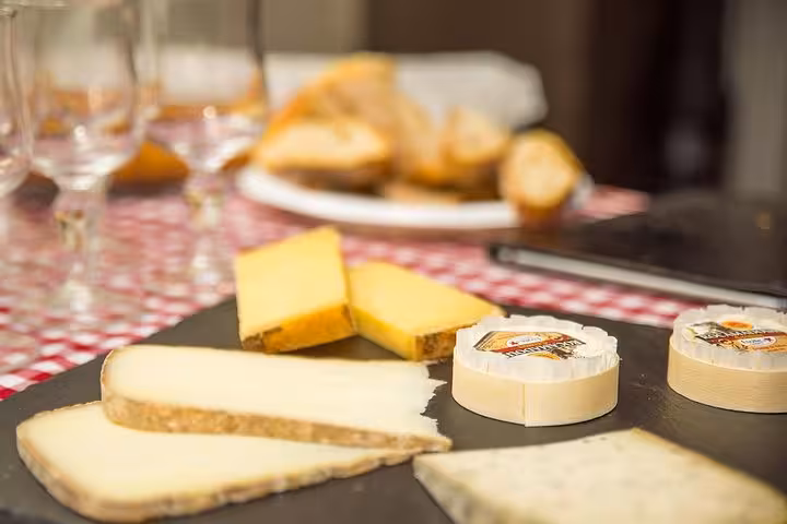 A selection of French cheeses on a slate board with bread and wine glasses in the background at Les Halles Paul Bocuse.
