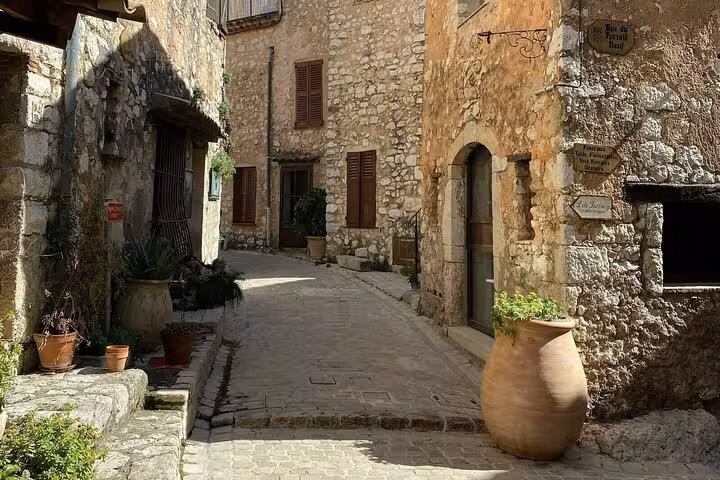 Rustic stone alley in a French Riviera perched village, featuring traditional architecture and potted plants.