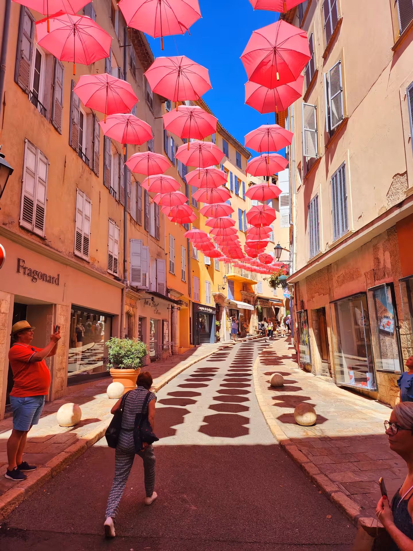 Colorful umbrellas hang above a quaint street in the French Riviera, creating a whimsical and vibrant atmosphere.