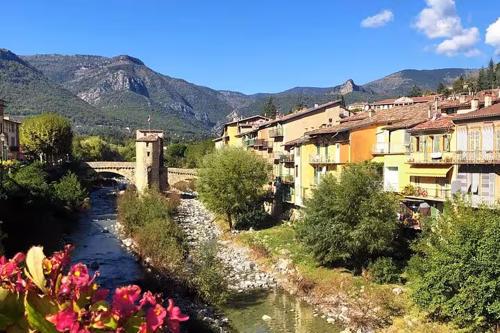 Charming French Riviera village by the river with colorful buildings and mountain backdrop on a sunny day.