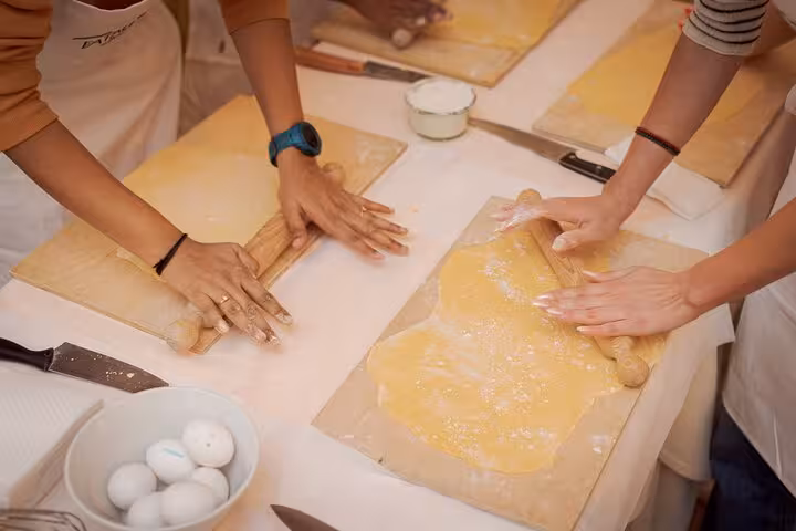 Close-up of hands rolling fresh fettuccine dough during a pasta class in Rome's Piazza Navona.