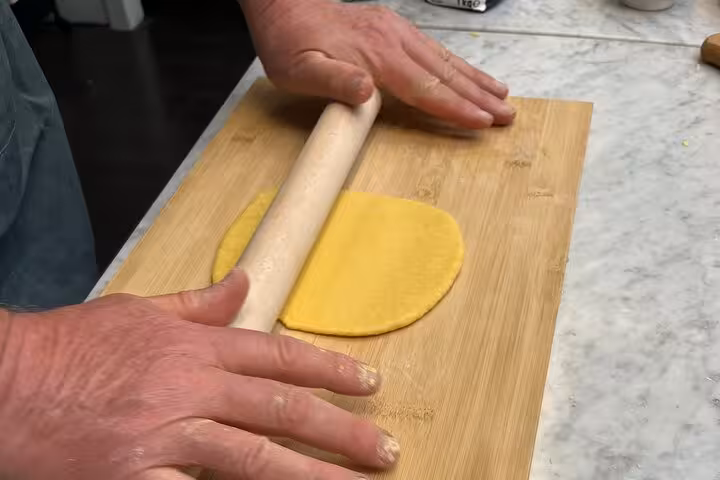 Close-up of hands expertly rolling fresh pasta dough on a wooden board, part of a fettuccine cooking class experience.
