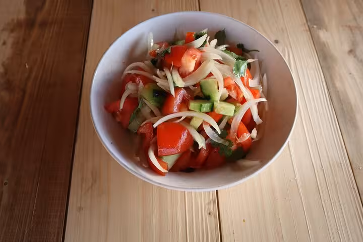 Fresh Portuguese salad with tomatoes, onions, and cucumbers in a white bowl, showcasing vibrant terrace cuisine flavors.