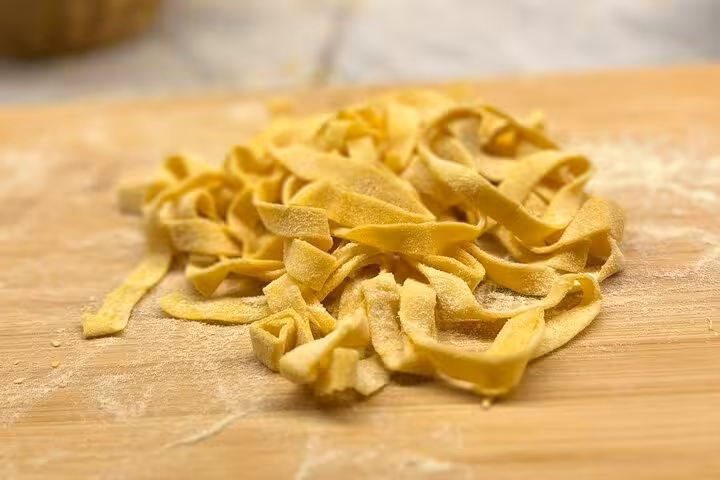 Freshly cut fettuccine pasta on a wooden board ready for cooking in an Italian culinary class.