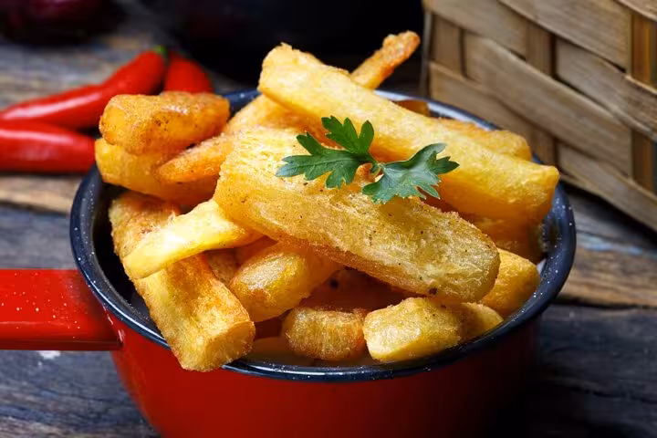 Golden fried yuca garnished with parsley in a red pot, perfect for Rio's Cookin' Good culinary tour.