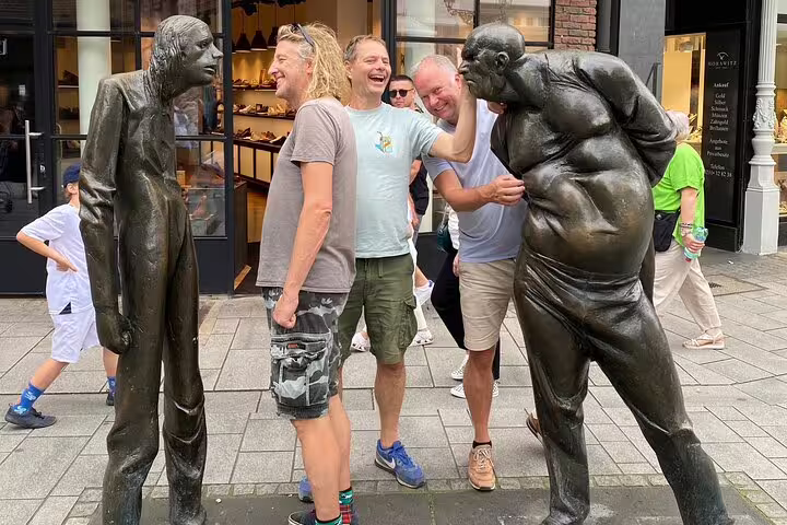 Friends posing between bronze statues in Düsseldorf on a scavenger hunt and sights self-guided city walking tour
