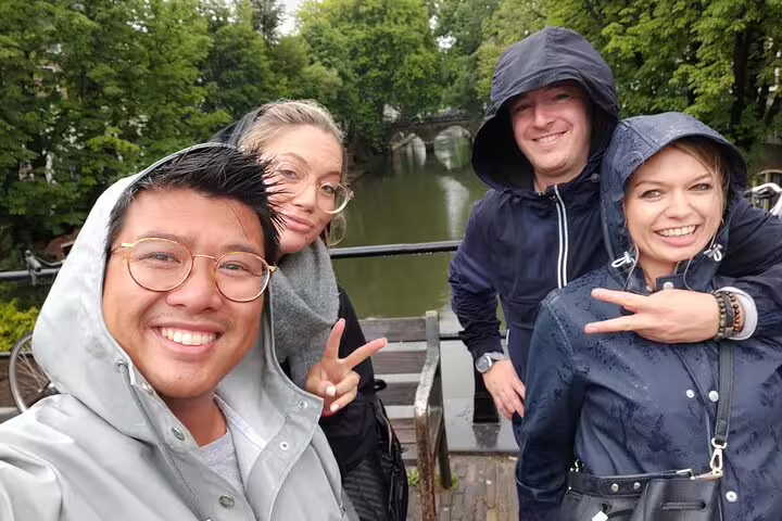 Friends in raincoats on a canal bridge during Copenhagen e-scavenger hunt, exploring at their own pace