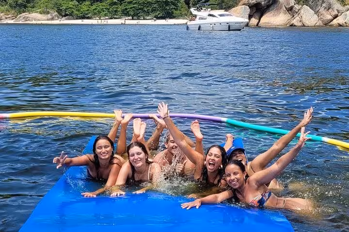 Friends splashing on floating mat during Velas do Rio private catamaran sailboat tour with open bar