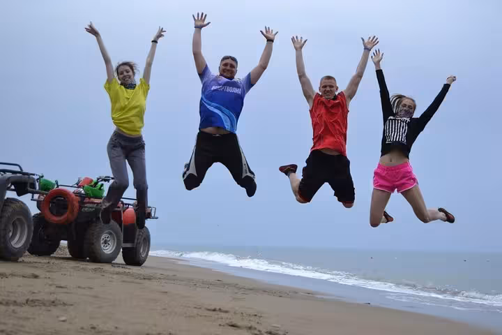 Friends jumping on the beach near parked ATVs after an Antalya Quad Safari, fun seaside off-road experience