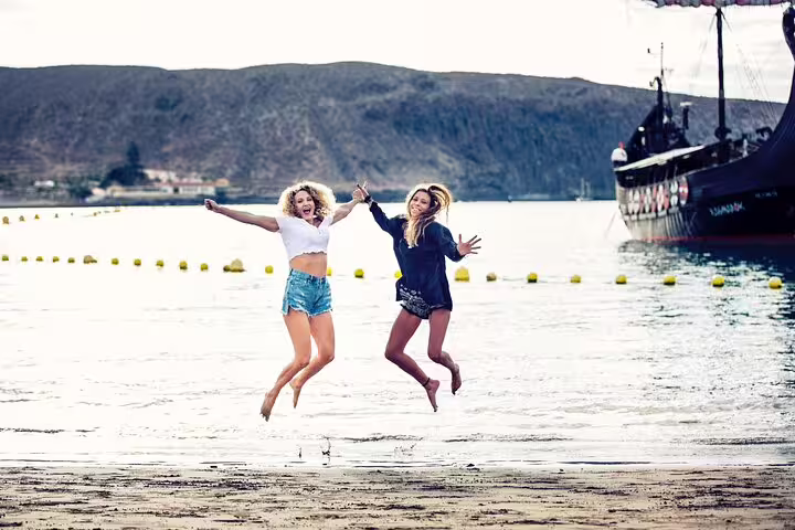Friends jumping on Tenerife shoreline with pirate ship backdrop in a fun private photoshoot with photographer