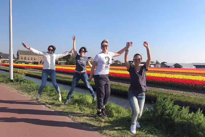 Friends jumping by vibrant tulip fields in Holland, enjoying a spring electric bike tour photo stop