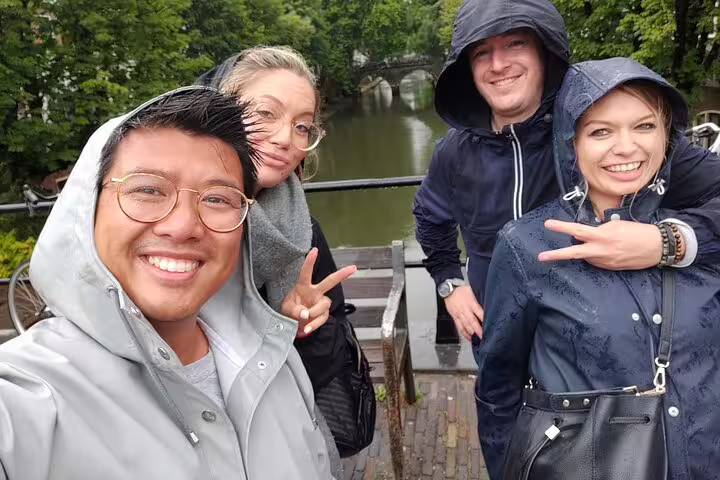 Friends in raincoats by Prague canal on self-guided e-scavenger hunt, exploring city clues at own pace