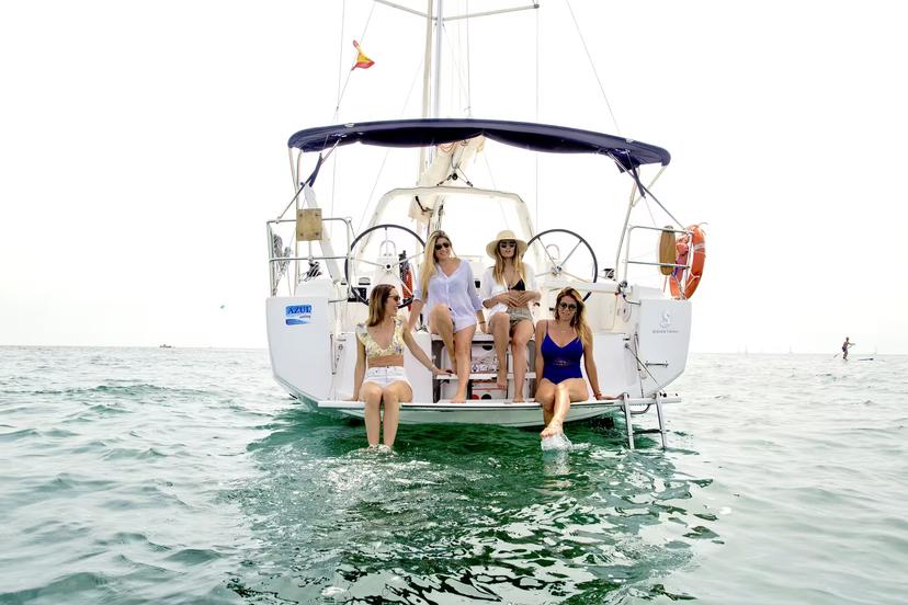Friends lounging on the back of a sailboat in Barcelona, swimming stop with open bar and snacks included