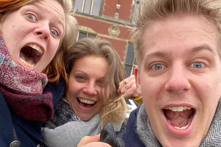 Friends taking a selfie in Amsterdam on an e-scavenger hunt, smiling during a self-guided city game
