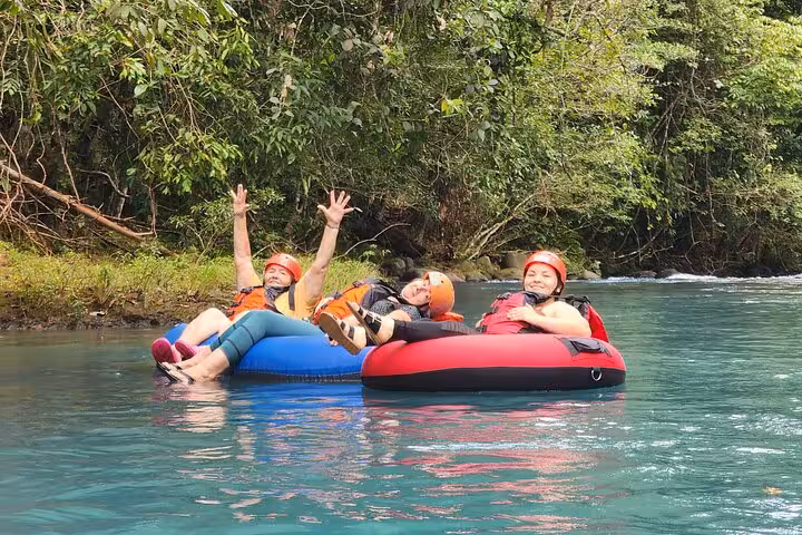 Three friends relaxing on inner tubes in the serene Celeste River, enjoying a scenic adventure amidst Costa Rica's nature.