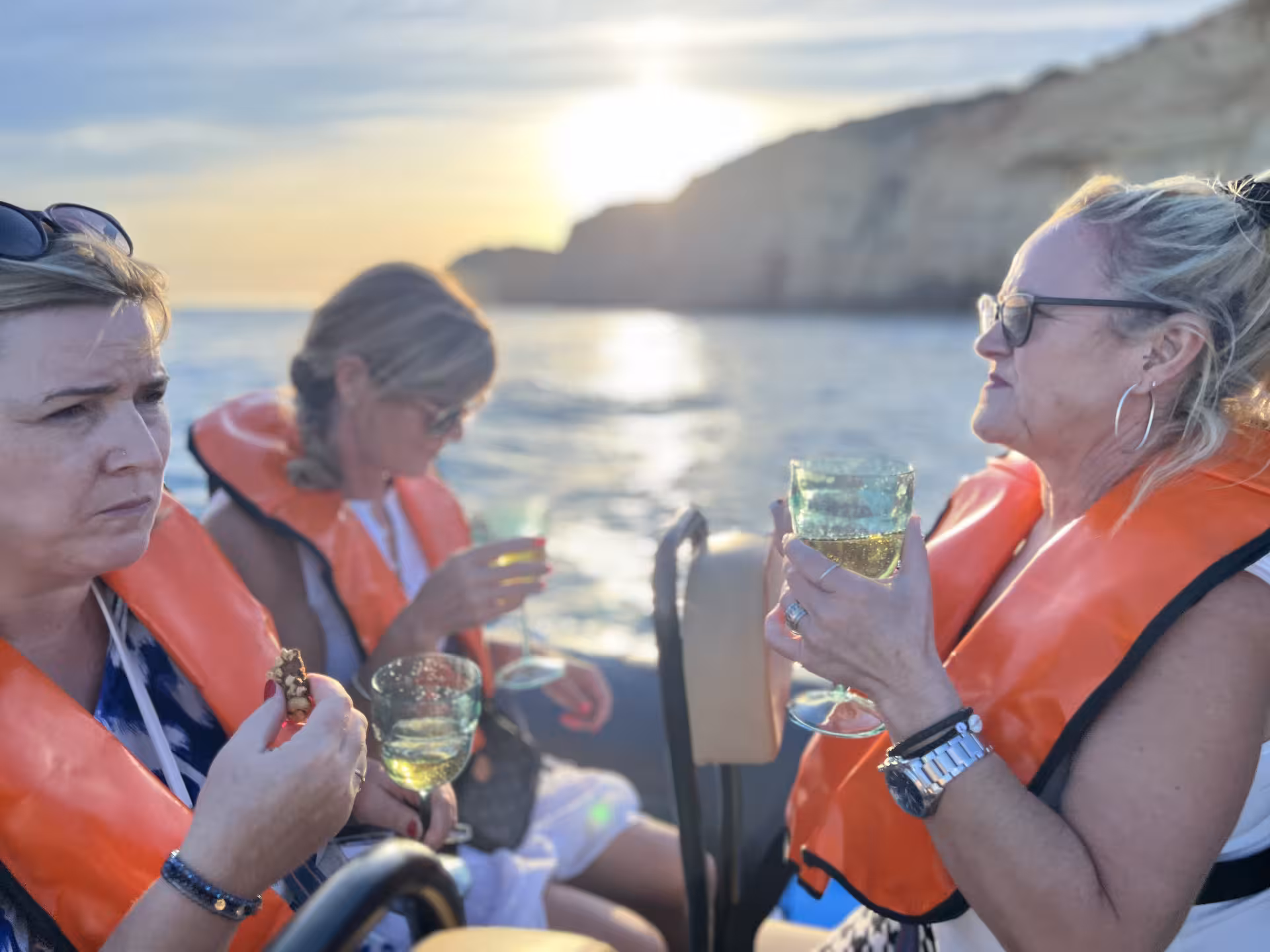 Friends in life jackets sipping chilled white wine at sunset on a tailor-made coastal boat charter