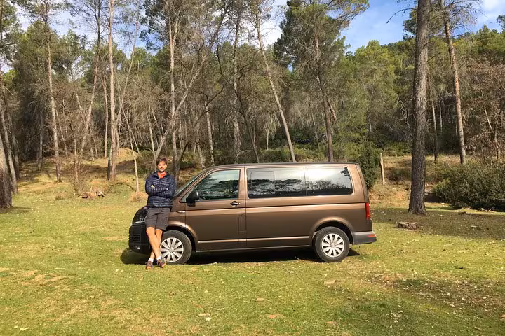 Man leans against a tour van in a lush forest setting, ready for a Frigiliana hike and wine tasting adventure from Málaga.