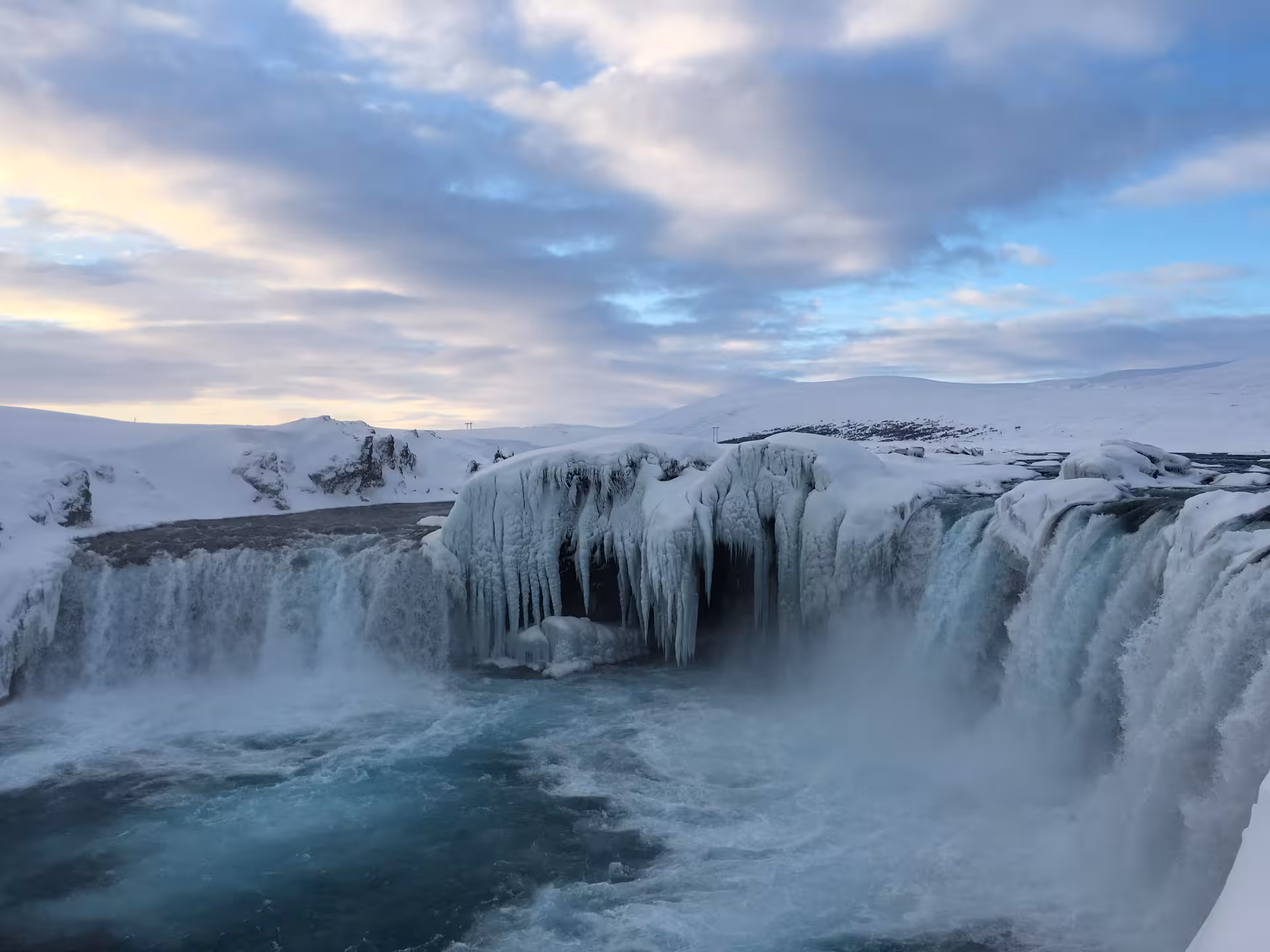 Majestic frozen waterfall with icy cascades under a vibrant sunrise sky, ideal for a private Icelandic winter tour.